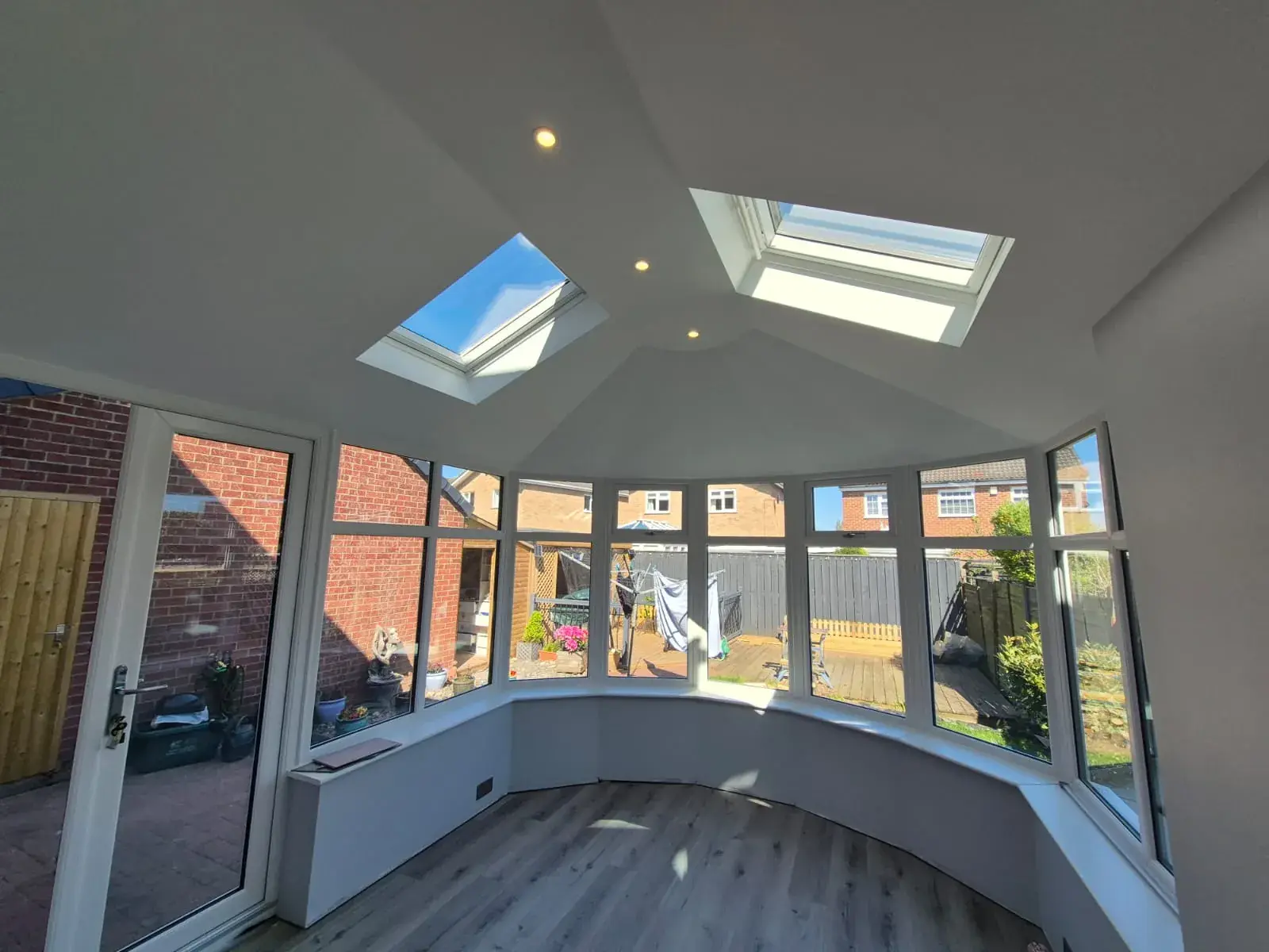 Inside a converted conservatory: plastered vaulted ceiling with downlights and two Velux roof windows above white uPVC windows