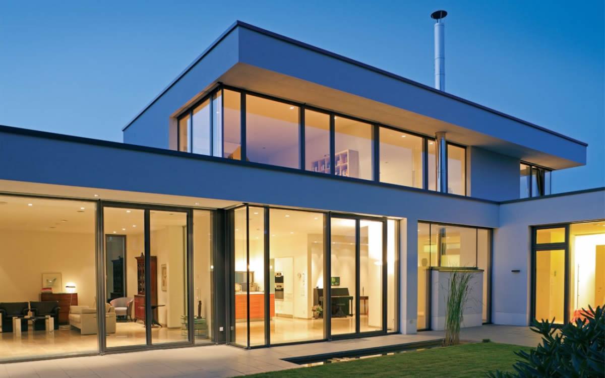 Modern house with large anthracite aluminium windows at dusk, warm light inside