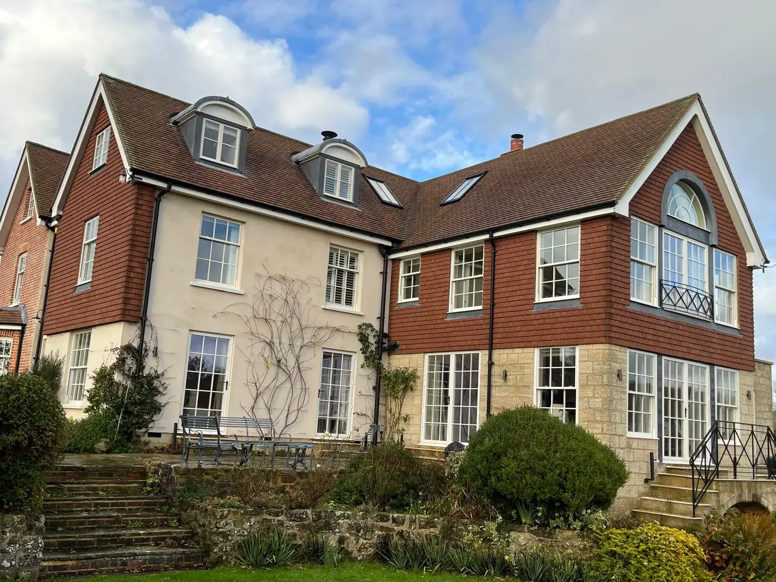 Large tile-hung Sussex house with white sash windows, French doors and an arched feature window above a garden terrace